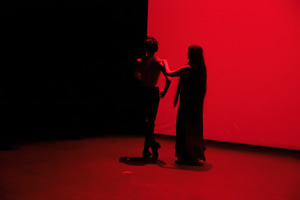 Dos intérpretes de Memoria en Movimiento bailan en silueta sobre un escenario iluminado en rojo.